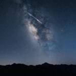 Beautiful night sky featuring the Milky Way galaxy and a shooting star over mountain silhouettes.