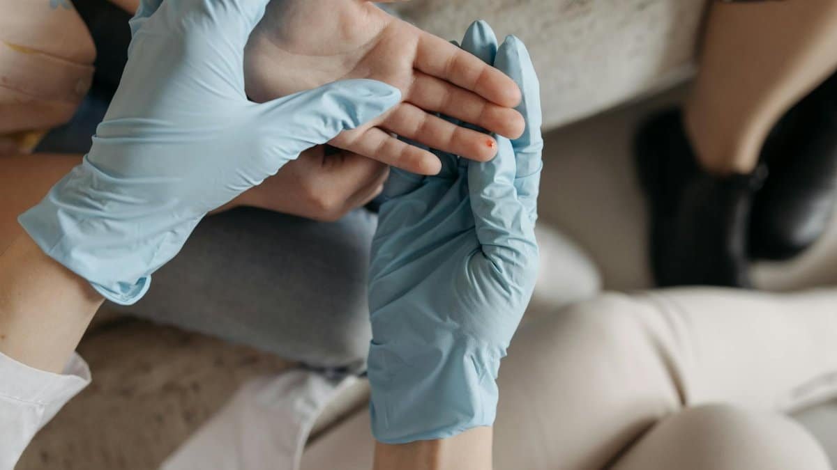 A medical professional wearing blue gloves examines a small wound on a person's finger indoors.