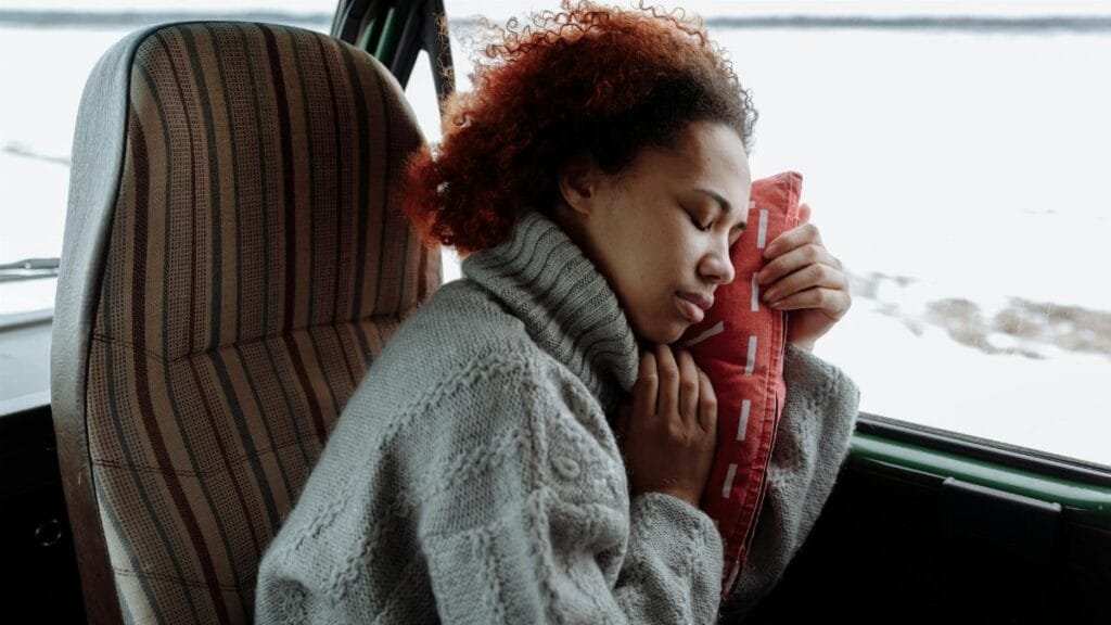 A peaceful moment of a woman sleeping in a campervan, wrapped in a cozy sweater during a winter road trip.