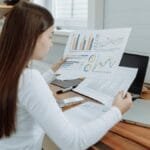 Woman reviewing business charts in a home office setting, showcasing remote work lifestyle.