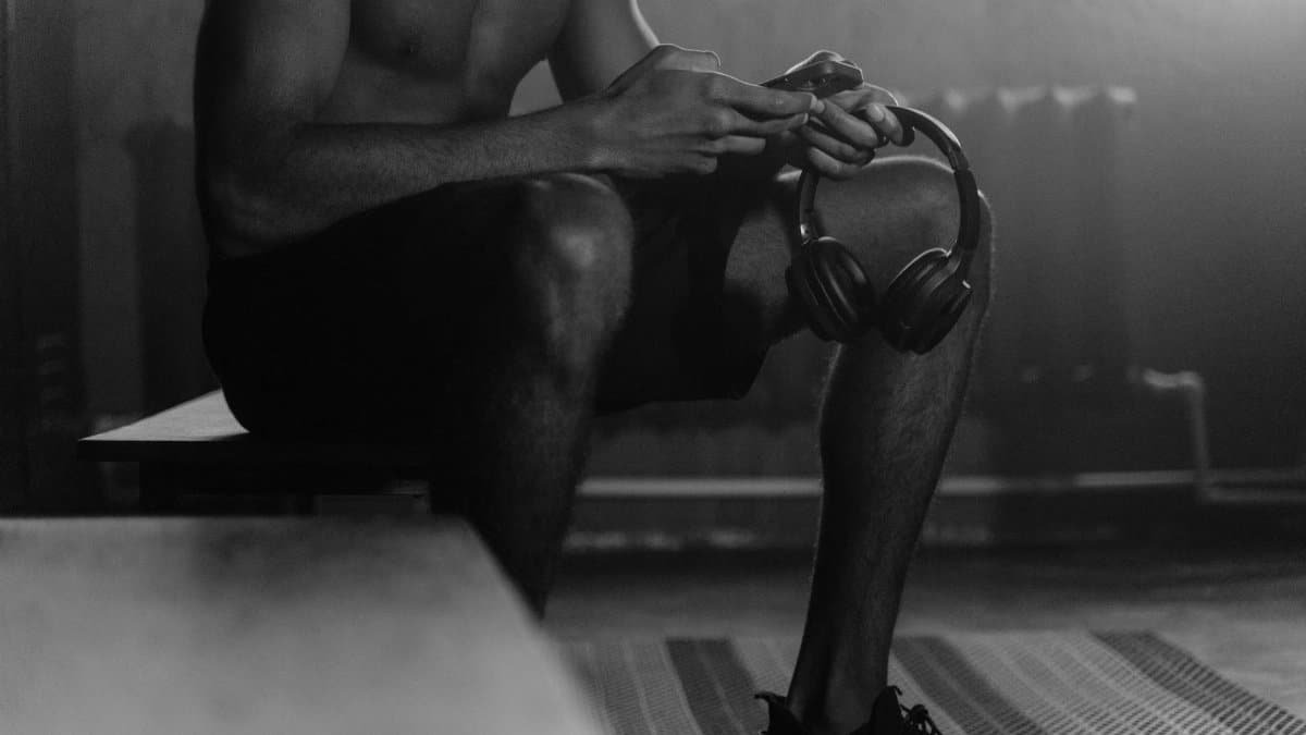 Monochrome photo of a man sitting on a gym bench holding headphones, evoking a quiet and focused atmosphere.