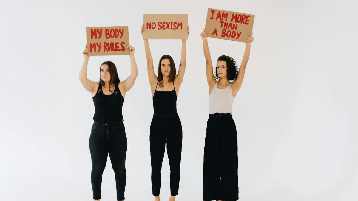 Three women holding feminist placards against sexism in a studio setting, promoting empowerment.