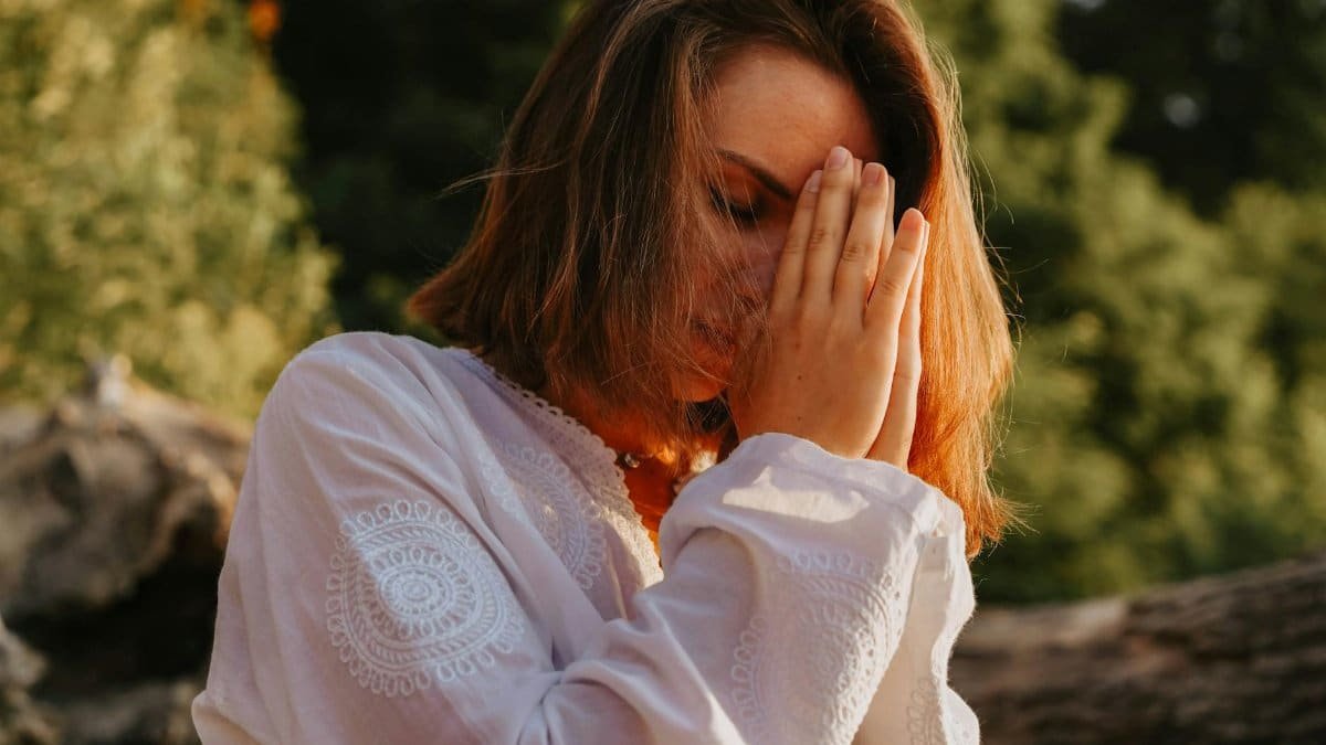 Woman meditating outdoors, eyes closed in peaceful prayer pose.