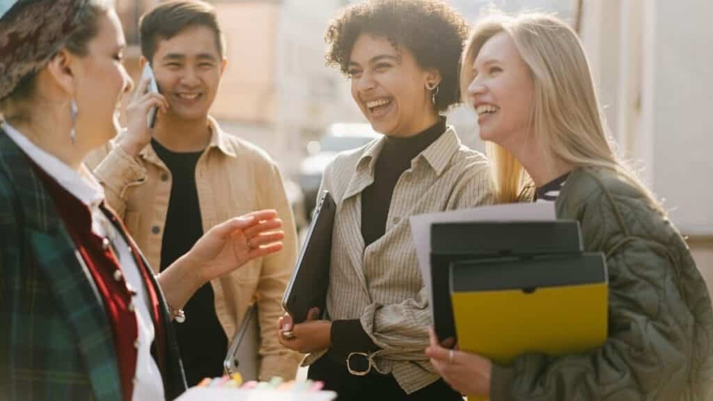 Group of adults laughing and conversing outdoors, capturing a joyful and diverse work environment.