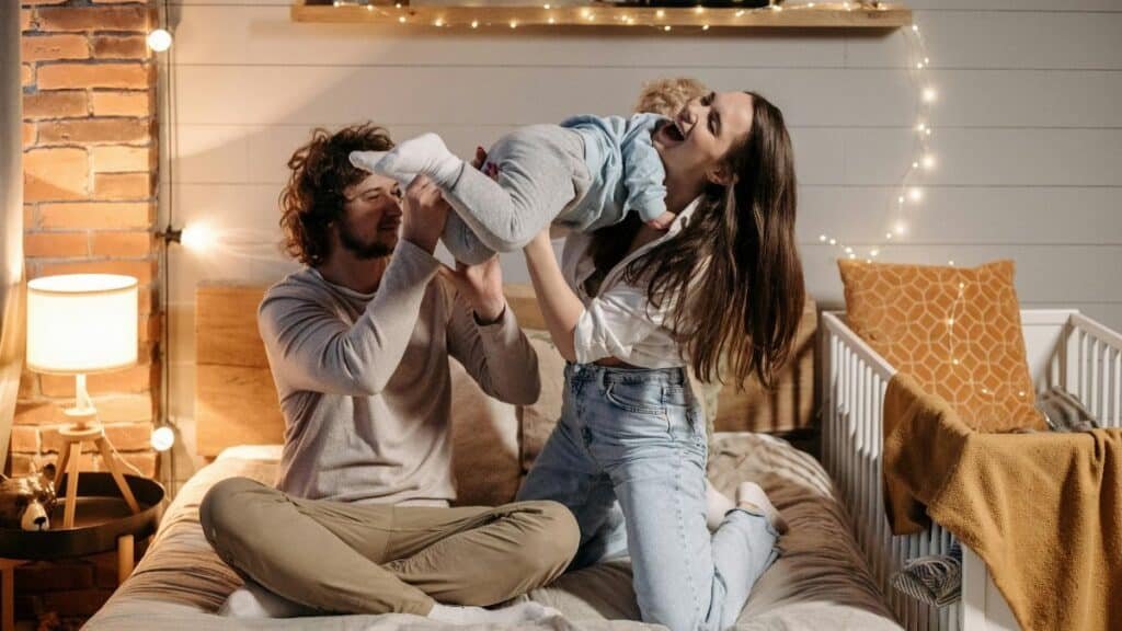 Joyful parents playing with their child on a bed in a warmly lit bedroom.