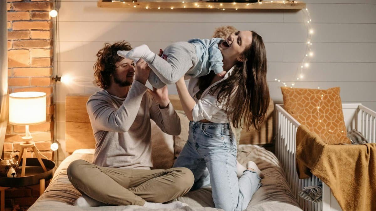 Joyful parents playing with their child on a bed in a warmly lit bedroom.
