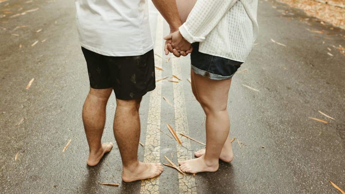 Barefoot expecting couple holding hands on a leaf-strewn road, symbolizing unity and anticipation.