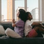 Interracial couple practicing meditation back-to-back on a couch. Calm and peaceful ambiance.