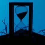 A silhouette of an hourglass set against a vivid blue background, highlighting the passage of time.
