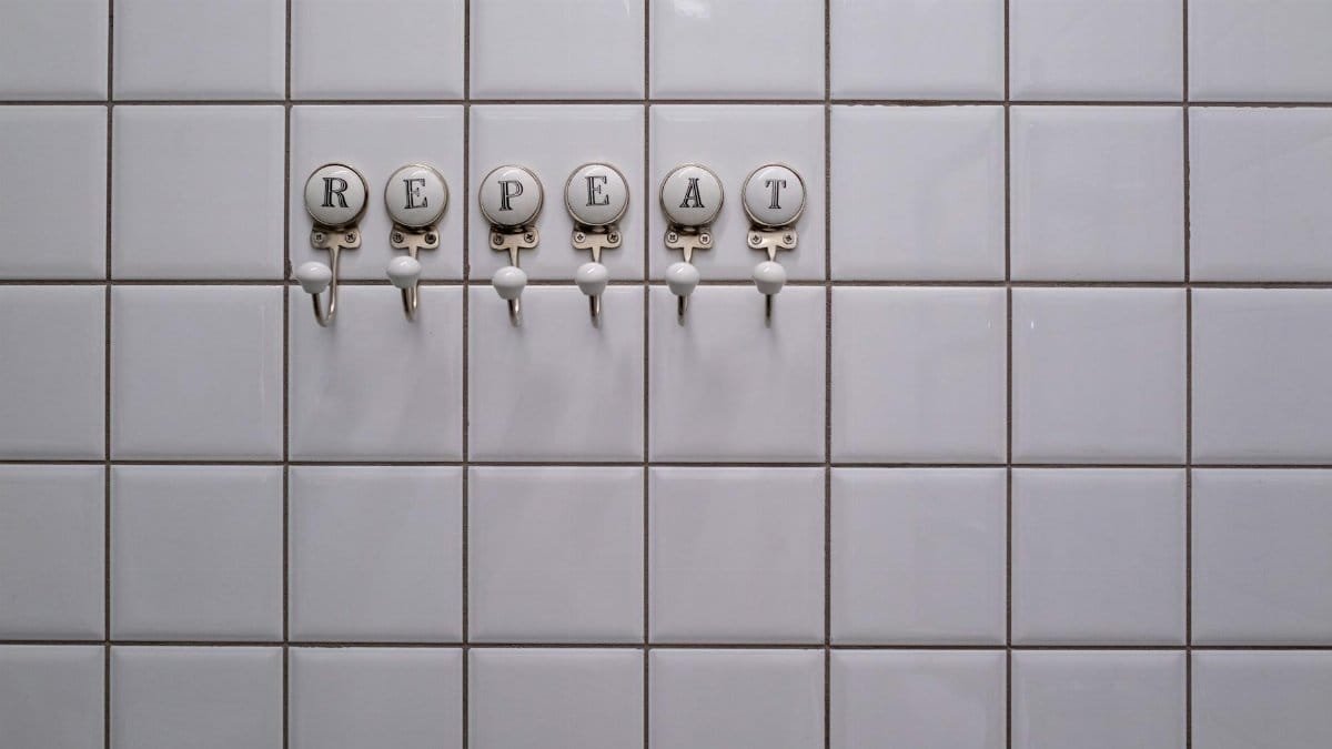 White tiled wall with towel hooks spelling 'REPEAT', showcasing a conceptual minimalist design.