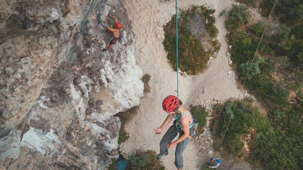 From above of anonymous people hanging on ropes while climbing on stony cliffs with green bushes