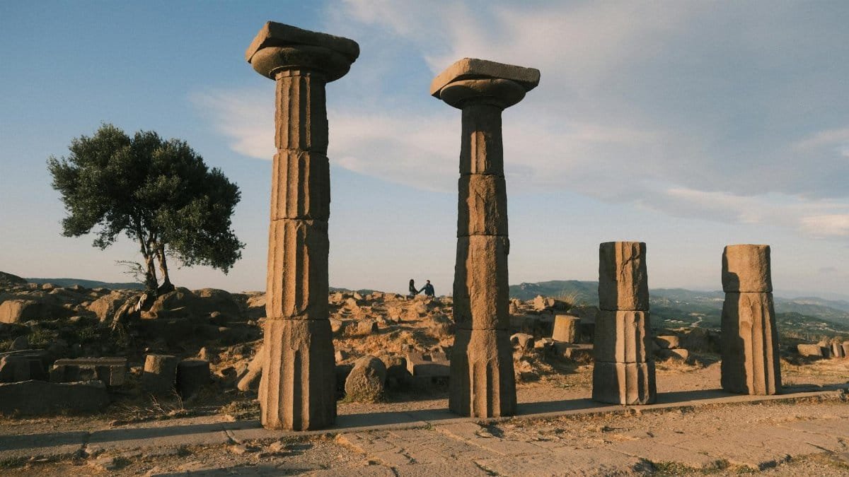 Explore the ancient ruins of Behramkale, Türkiye, under a warm sunset sky, capturing historical columns and landscape.
