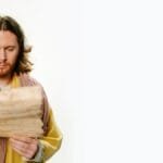 Man with long hair and beard reading an ancient scroll on a white background.