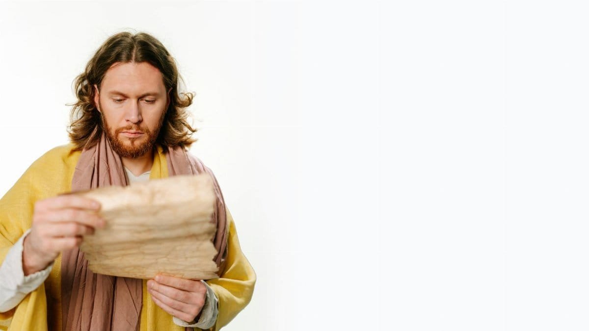 Man with long hair and beard reading an ancient scroll on a white background.