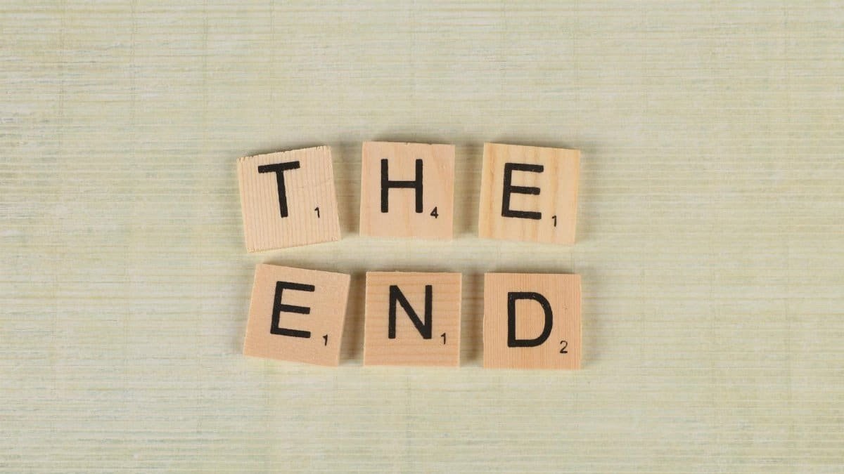 Close-up of Scrabble tiles spelling 'The End' on a simple wooden background for creative concepts.