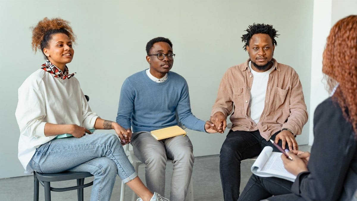 A diverse group of adults in a supportive therapy session, holding hands indoors.