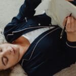 An adult woman relaxes while writing in a notebook with crumpled papers around her.