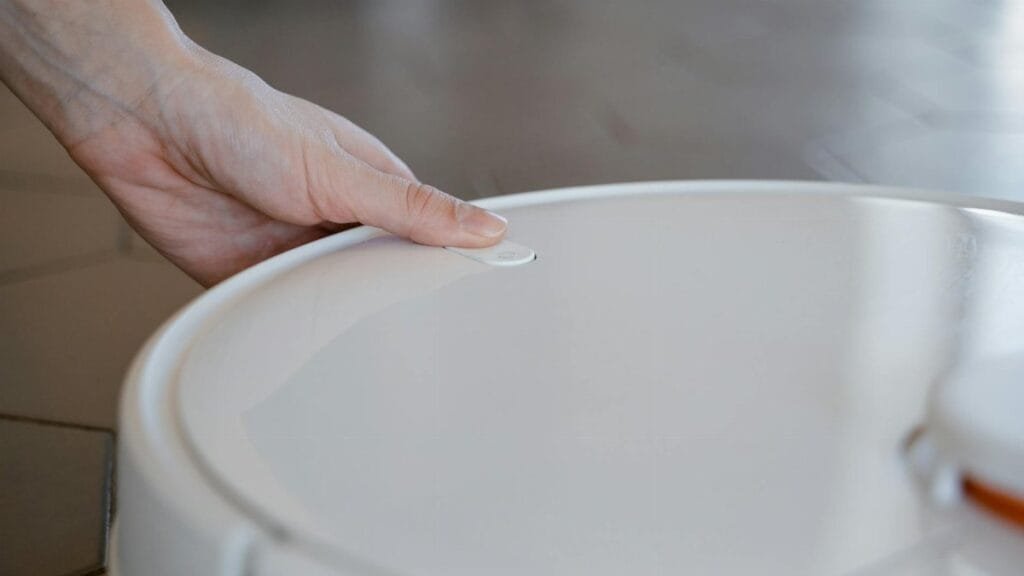 Close-up of a hand pressing a button on a robotic vacuum cleaner indoors.