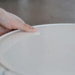 Close-up of a hand pressing a button on a robotic vacuum cleaner indoors.