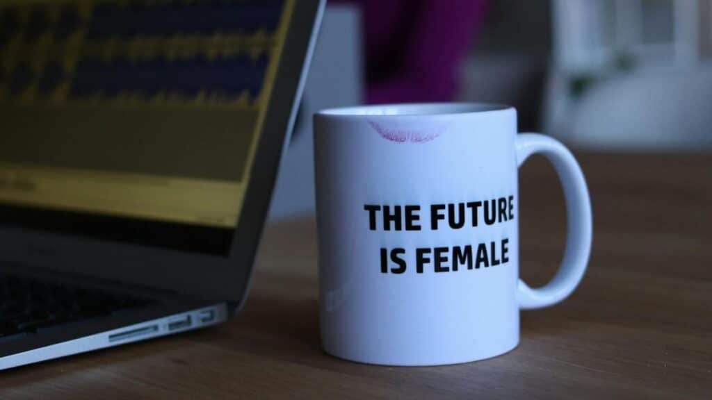 A white mug with 'The Future Is Female' beside a laptop, symbolizing empowerment.