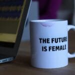 A white mug with 'The Future Is Female' beside a laptop, symbolizing empowerment.