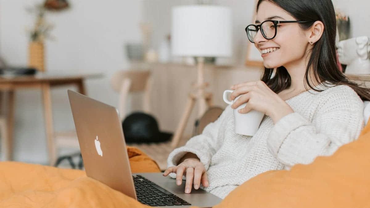 Woman enjoying a cozy moment with a laptop and coffee in a modern interior setting.