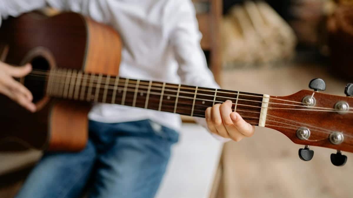 A close-up of a child practicing guitar chords indoors, emphasizing hands and strings.