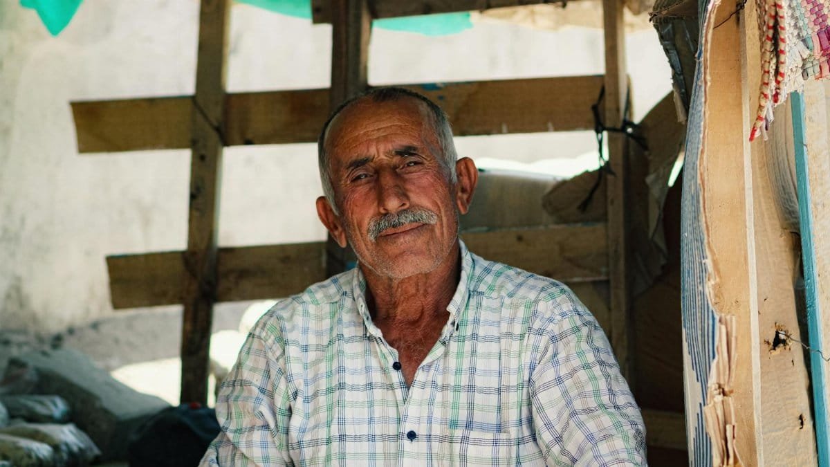 Senior man with mustache sitting in a rustic setting, exuding warmth and wisdom.