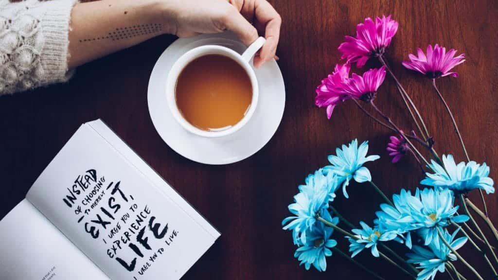 A cozy setup with tea, flowers, and an inspirational quote book on a wooden table.