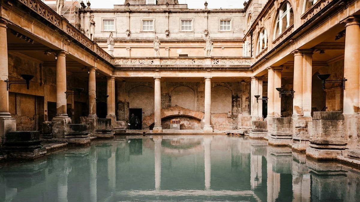 Exterior of worn out medieval stone building with columns located near canal with reflection on water surface in old city
