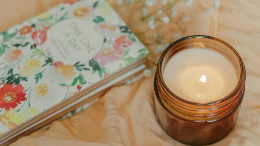Floral journal and warm candle on soft fabric, creating a cozy atmosphere.