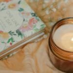Floral journal and warm candle on soft fabric, creating a cozy atmosphere.