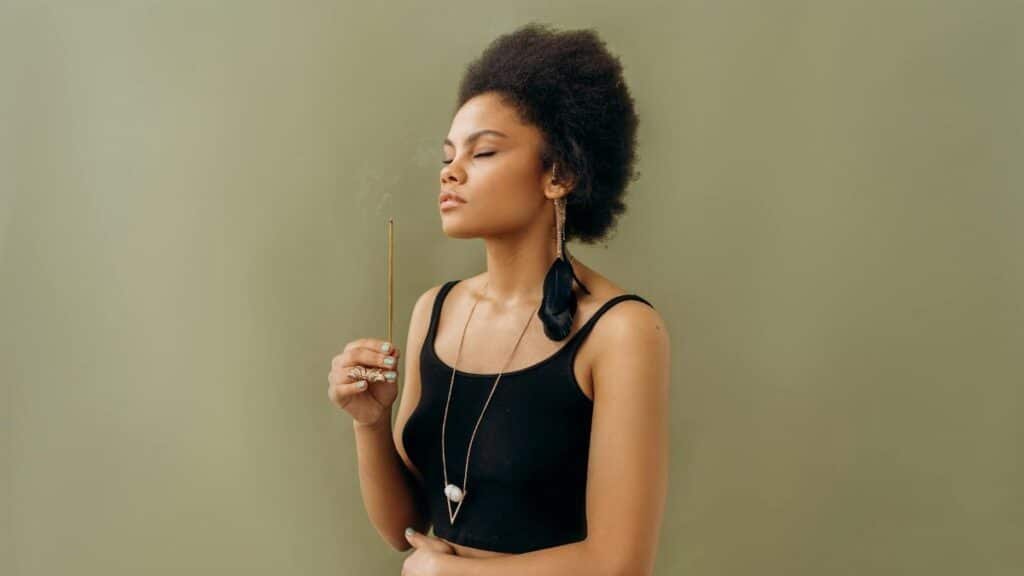 Serene young woman practicing aromatherapy with incense stick indoors, promoting wellness.