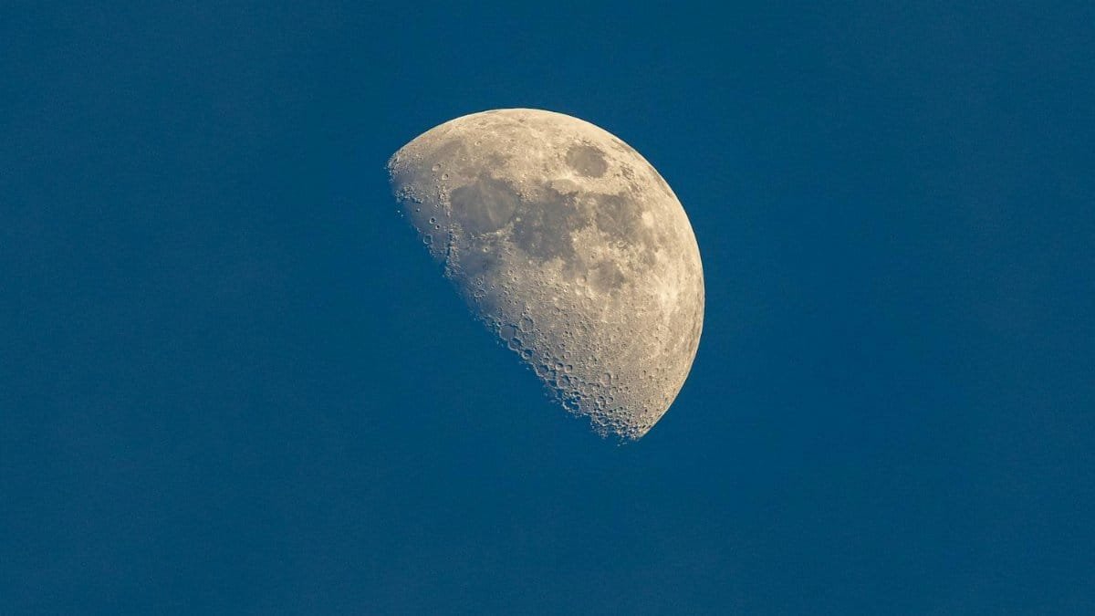 A detailed half moon against a clear blue sky captured during twilight.