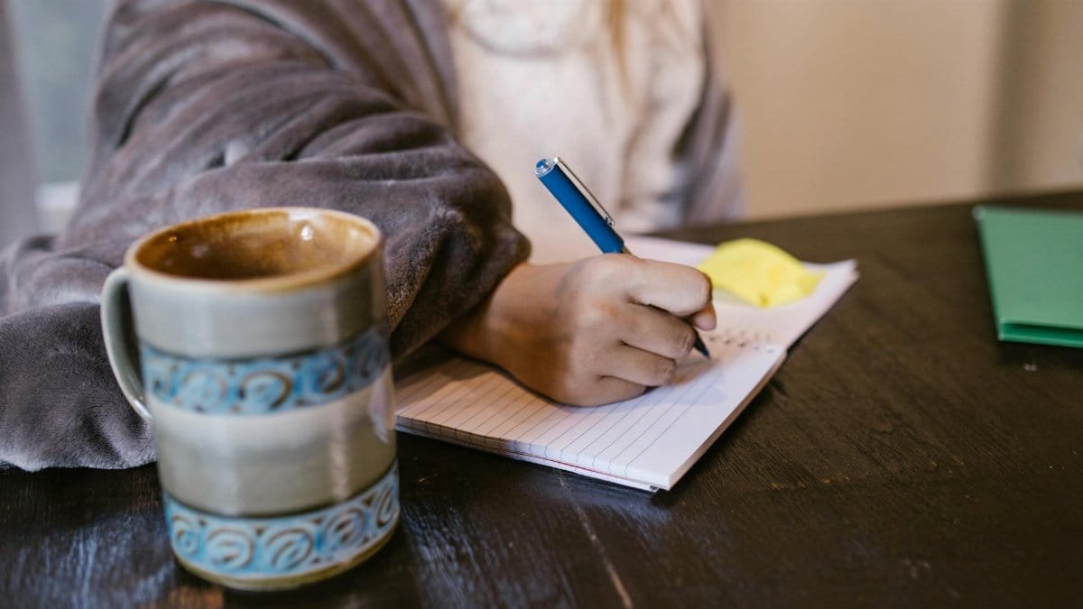 A person comfortably writing in a notebook while enjoying a cup of coffee indoors.