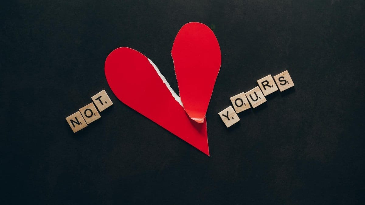 A torn red heart with 'Not Yours' spelled in Scrabble tiles on a black background.