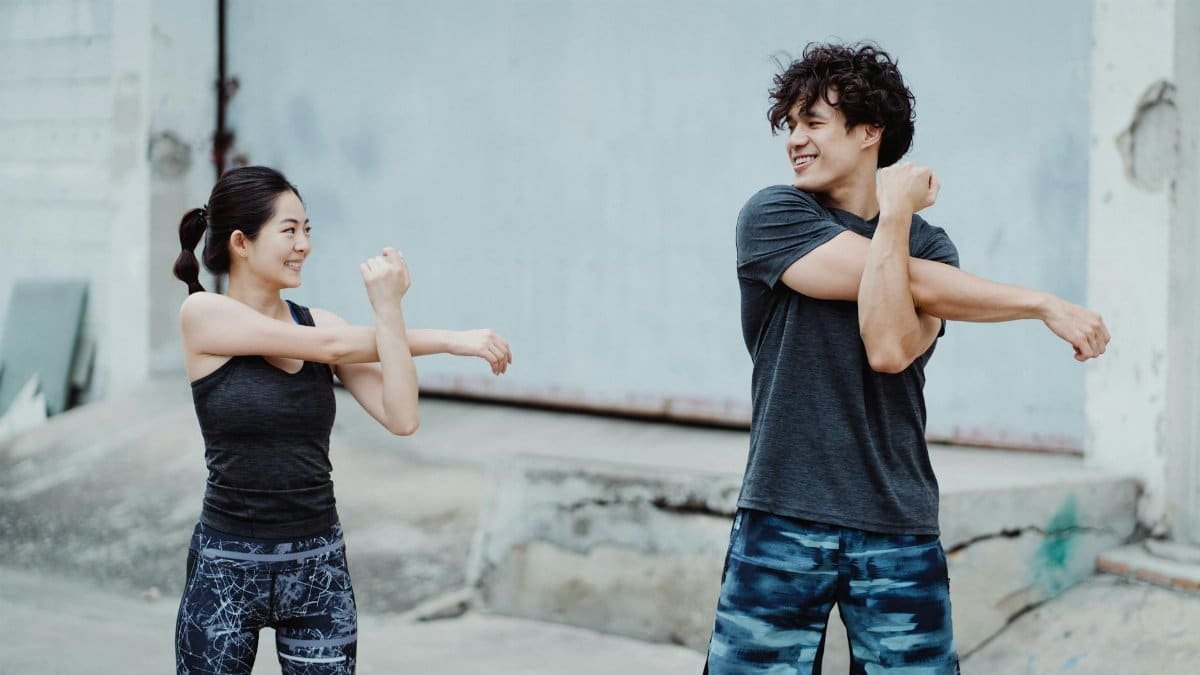 Couple engaging in a warm-up stretch outdoors. Emphasizes health and fitness.
