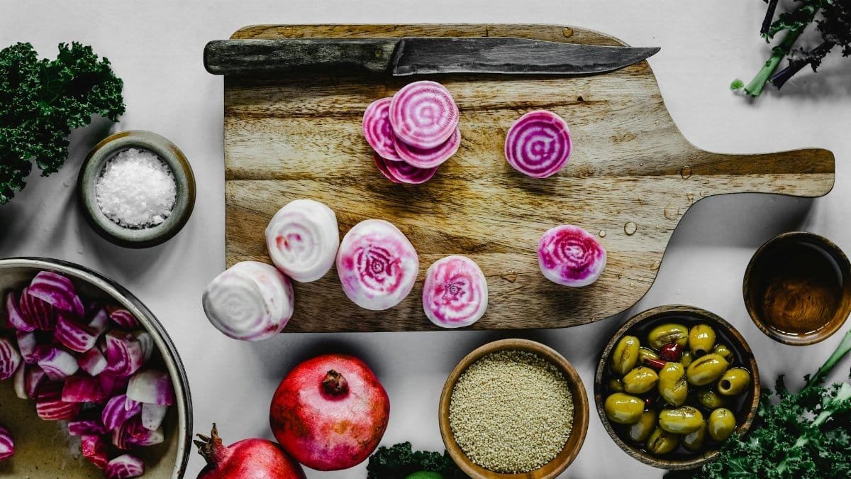 Top view of colorful chioggia beets on a wooden cutting board, surrounded by healthy ingredients like kale and olives.