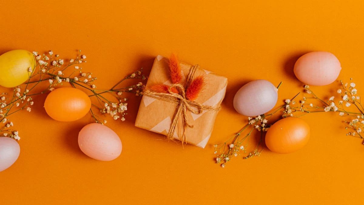 A vibrant arrangement of colorful Easter eggs, flowers, and a wrapped gift on an orange background.