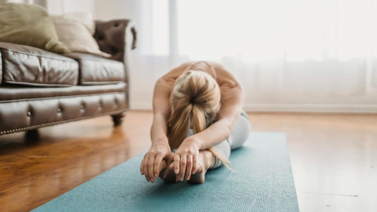 A woman performs a yoga stretch on a mat in a cozy living room, embracing wellness and relaxation.