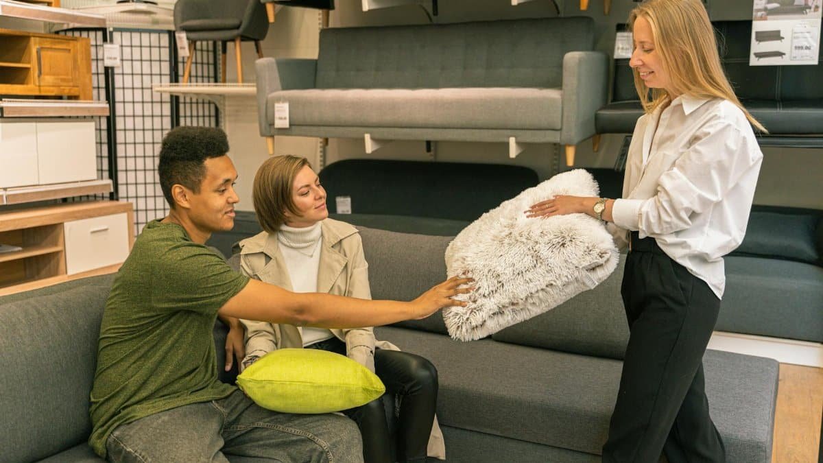 A couple explores pillow options with a saleswoman in a modern furniture store.