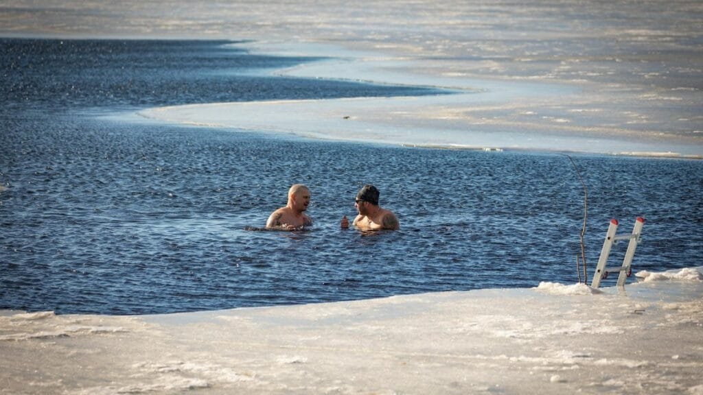 Two men brave the cold for a swim in a partially frozen lake during winter.