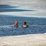 Two men brave the cold for a swim in a partially frozen lake during winter.