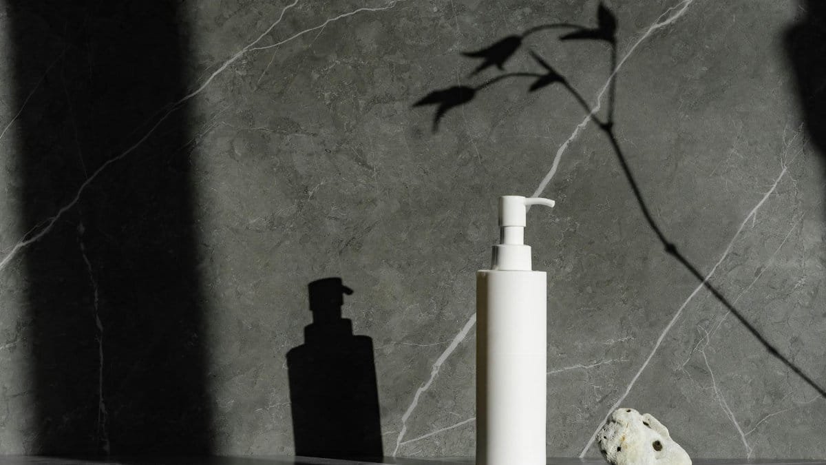 Sophisticated white pump bottle on gray marble with natural shadow play, ideal for skincare branding.