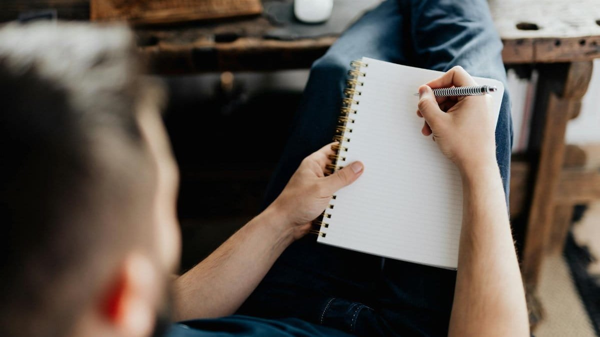 Man lying back and writing on a notebook, relaxing at home. Cozy setting with a rustic desk.