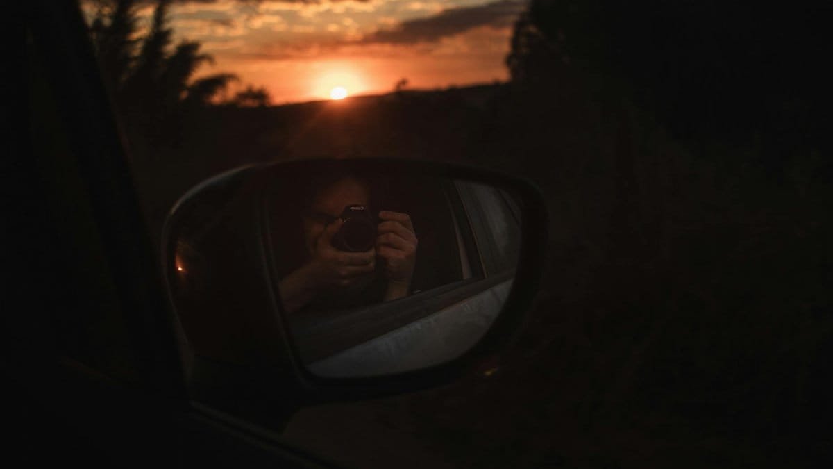 A mesmerizing sunset captured in a car side mirror with a camera reflection.