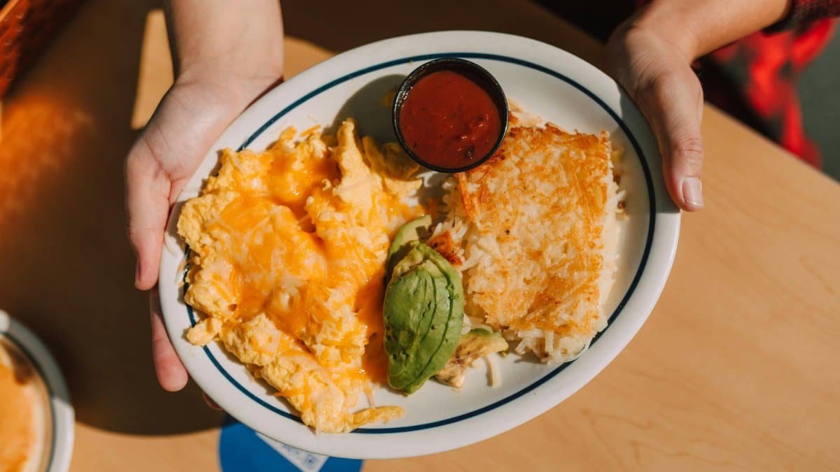 Plate of cheesy scrambled eggs, avocado, hash browns, and sauce, perfect for breakfast.