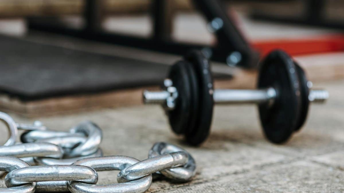 Close-up of a metal dumbbell and heavy chain on a gym floor, symbolizing strength and fitness.