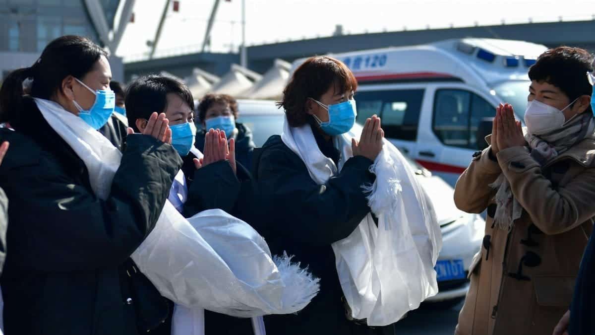 Healthcare workers wearing masks exchange respectful gestures in front of ambulances.