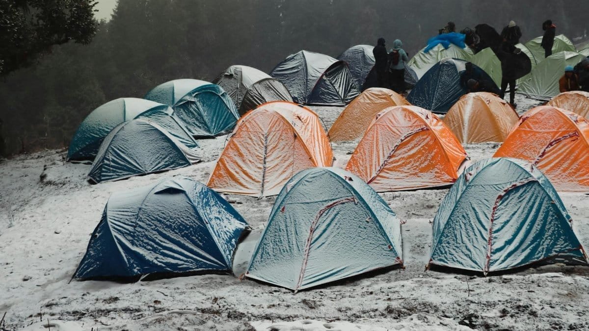 A vibrant campsite with colorful tents in a snowy forest in Singtur Range, India, capturing the essence of winter camping.